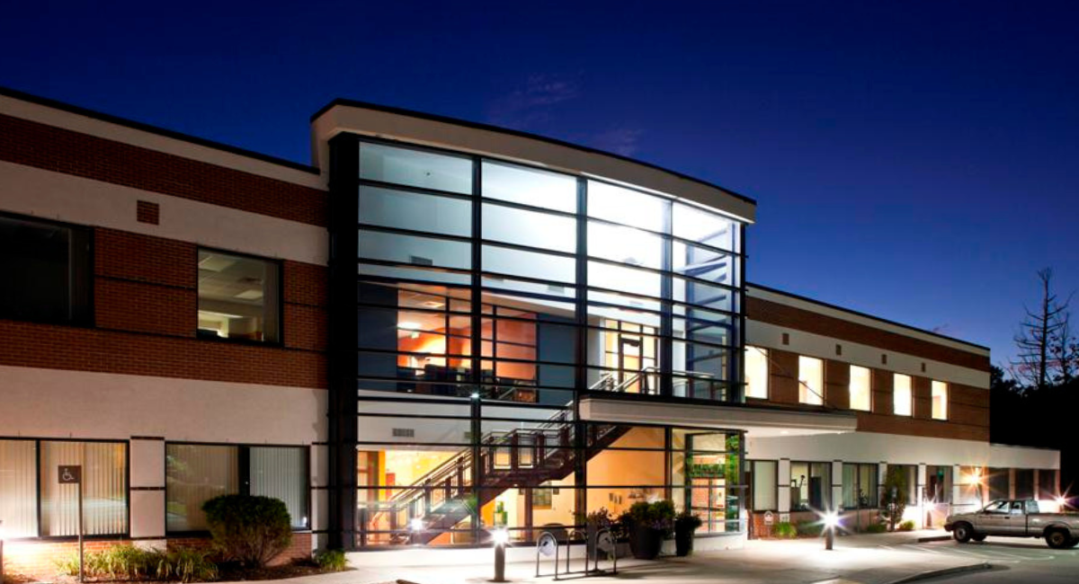 Exterior of Monadnock Community Hospital at dusk with large glass windows lit from inside; overlaid text reads "Your Hospital" in bold white script.