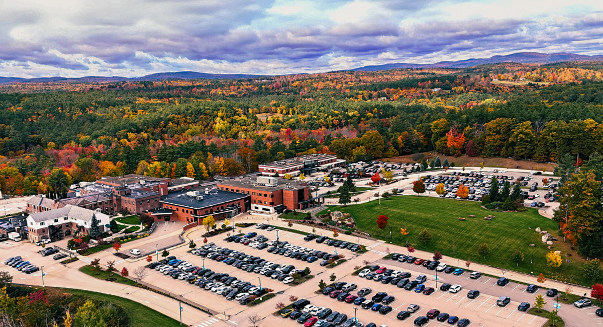 Aerial image of Monadnock Community Hospital’s full campus surrounded by autumn foliage, parking lots, and green lawn, with rolling mountains in the distance.