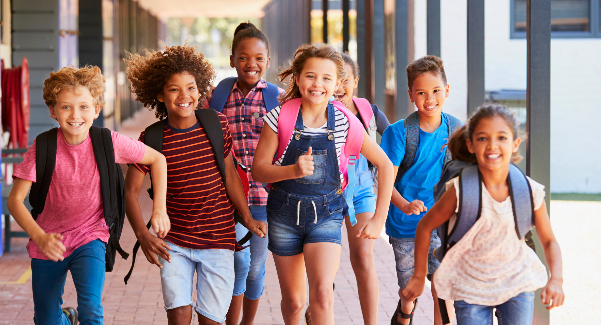 Happy children with backpacks and big smiles running at school