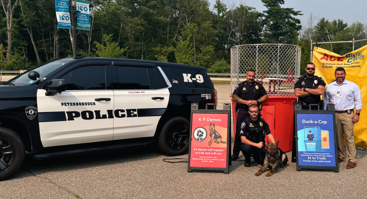 Peterborough Police officers and MCH security manager pose with a K-9 dog in front of their vehicle and a dunk tank, with signs for K-9 demonstrations and Dunk-a-Cop.