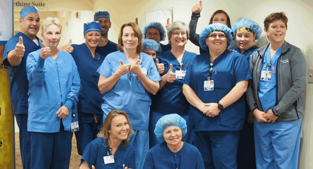 Group of Monadnock Community Hospital staff in blue scrubs smiling and giving thumbs up beside a gold banner that reads “Quarterly Award Winner for Exceptional Patient Experience.”