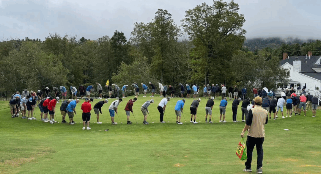 Dozens of golfers lined up in a large circle on the green, bending over their putters in a fun, synchronized moment.