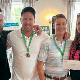 Four golfers, wearing medals and holding their prize envelope, smile together after winning the tournament.