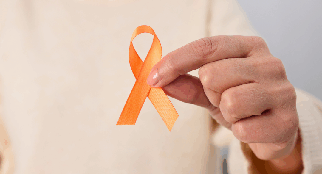 Close-up of a hand holding an orange awareness ribbon, representing support and awareness for multiple sclerosis.