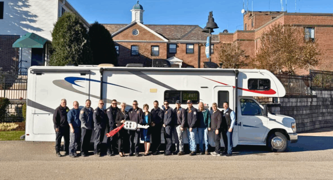 Group of Monadnock Community Hospital and local fire department members standing in front of a large white RV, marking the donation of the vehicle to the Fire Chiefs Association.