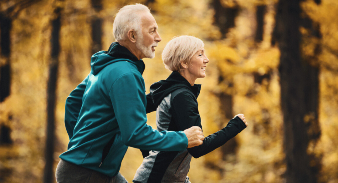 Older couple walking briskly together on a wooded trail in autumn, representing active recovery, mobility, and healthy aging through rehabilitation.