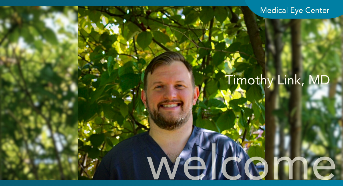 Timothy Link, MD, ophthalmologist at The Medical Eye Center, smiling outdoors in navy scrubs with green trees in the background