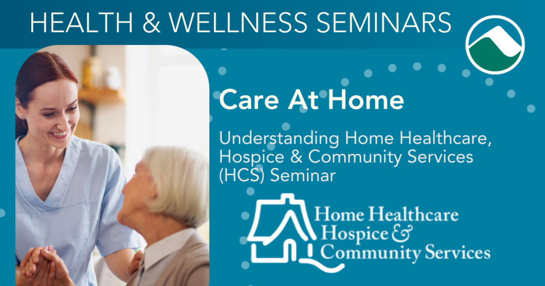 A smiling healthcare caregiver in blue scrubs sits close to an older adult, holding their hands and making eye contact in a warm, home-like setting, representing supportive care and connection.
