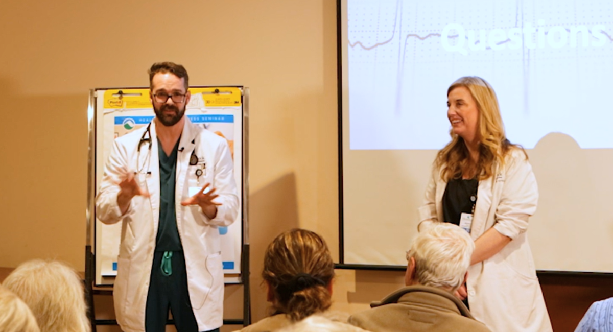 Robert Spencer and Brooke OConnor of Monadnock Cardiology Associates present at the Keeping the Beat Understanding Atrial Fibrillation seminar at Monadnock Community Hospital Dr Spencer gestures while speaking to attendees with a projection screen displaying the Q and A slide in the background