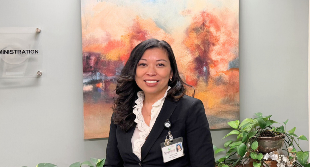 A professional headshot of a hospital leader standing in front of artwork and a plant indoors