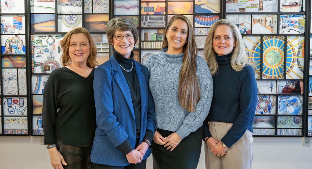 The Monadnock Community Hospital Philanthropy Team stands together in front of a colorful artwork display. From left to right are Katharyn Ernst, Laura Gingras, LeeAnn Moore, and Amy Theriault, smiling for a group portrait.