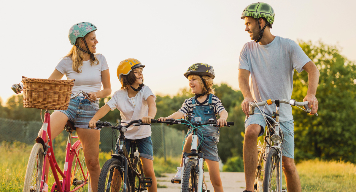 Family wearing bicycle helmets while standing with their bikes on a sunny outdoor trail