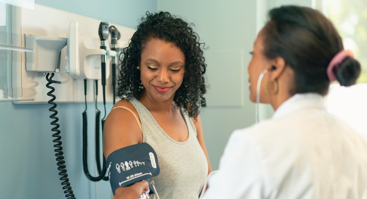 A woman has her blood pressure checked by a healthcare professional in an exam room.
