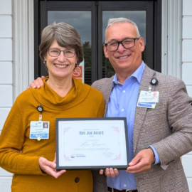Laura Gingras, MCH Vice President of Philanthropy and Community Relations, and President and CEO Richard Scheinblum smile while holding her 2026 Monadnock United Way Ken Jue Award outside the hospital's Parmelee Entrance.